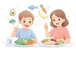 Uśmiechnięci chłopiec i dziewczynka siedzący przy stole z talerzami pełnymi zdrowego jedzenia.